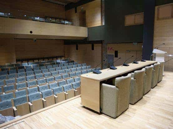 Interior del auditorio con butacas azules y escenario equipado para conferencias