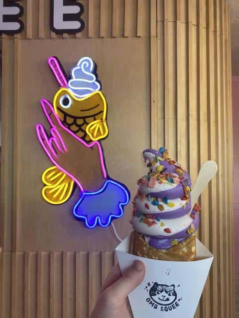 Helado de colores con topping de cereal junto a un letrero neón del logo de OMG Squee