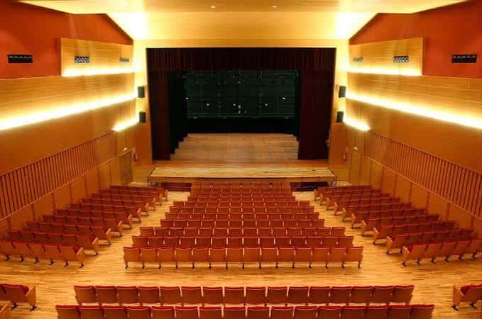 Interior del auditorio con butacas rojas dispuestas en gradas hacia el escenario principal