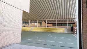 Pabellón deportivo con gradas amarillas y techo ondulado