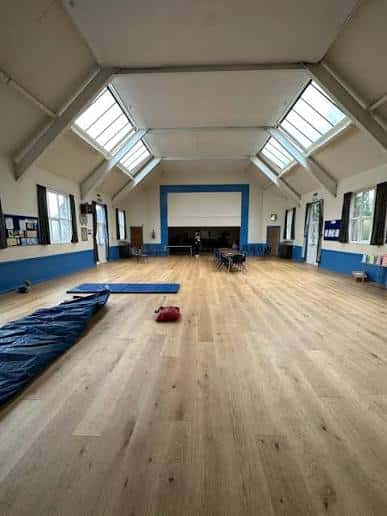 Interior del hall de eventos con suelo de madera, techo alto con claraboyas y espacio amplio para actividades