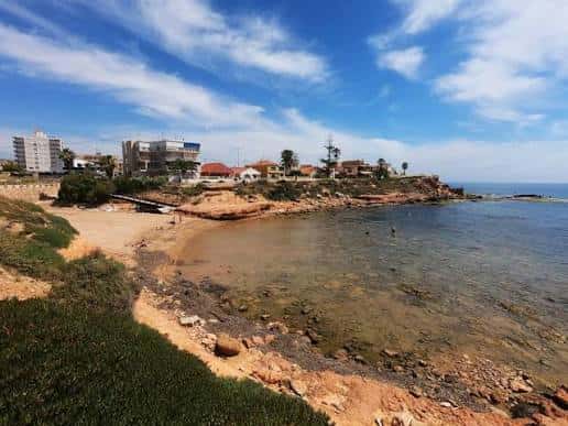 Playa de Cala de la Higuera con edificios residenciales al fondo y cielo despejado