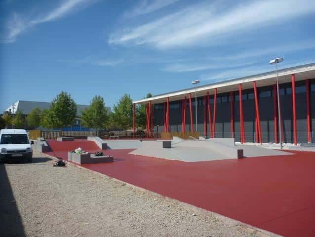 Plaza principal del skatepark con estructuras de concreto y edificio moderno al fondo