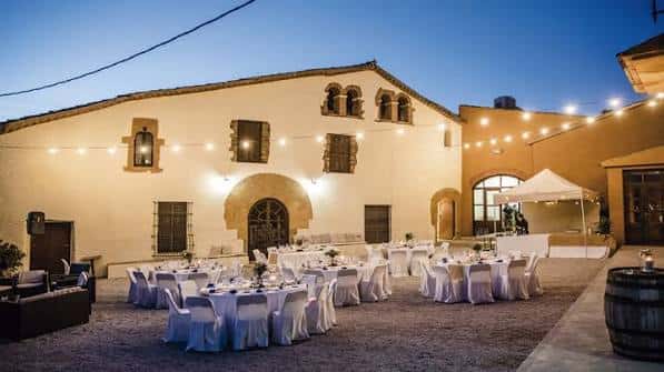Patio exterior de la masía decorado con mesas y sillas para una boda o evento al atardecer