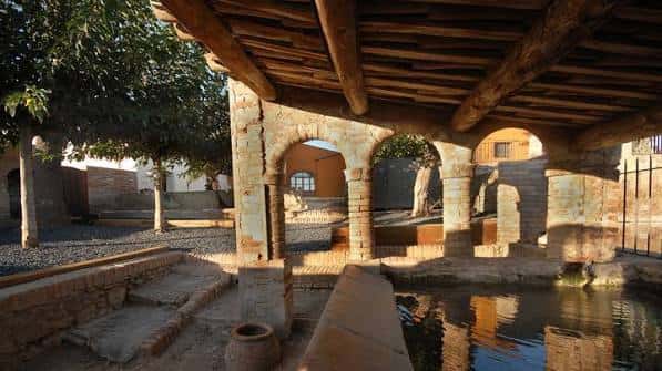 Área de patio interior con arcos de piedra, vigas de madera y un estanque decorativo