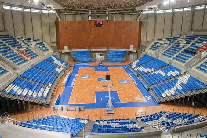 Interior vacío del pabellón mostrando la cancha de baloncesto y gradas azules