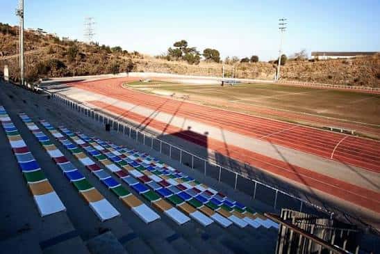 Gradas con asientos multicolores y vista al campo de atletismo
