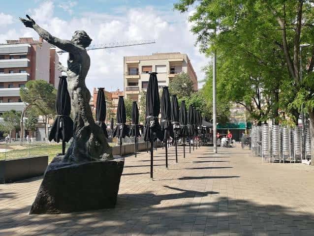 Plaza con escultura moderna y sombrillas plegadas, ideal para eventos al aire libre