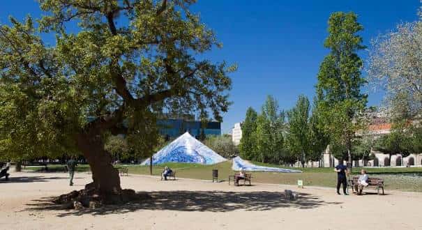 Vista panorámica del parque con el icónico elemento escultórico blanco y árboles frondosos bajo un cielo azul