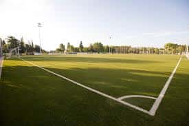 Campo de fútbol artificial con líneas blancas y porterías bajo cielo despejado