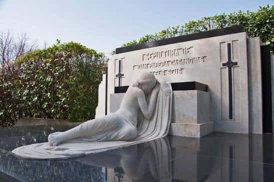Monumento funerario con escultura de mujer en actitud de lamento frente a una lápida con cruces