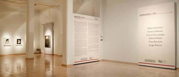 Vista general del espacio expositivo con paneles informativos y obras enmarcadas