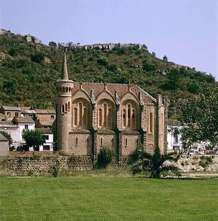 Vista exterior de la Iglesia de la Sagrada Familia de la Colonia Güell con su fachada neogótica y el monte de Collserola al fondo