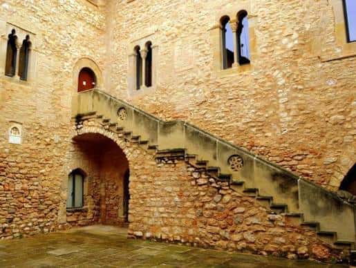 Patio de piedra con escalera exterior y ventanas góticas