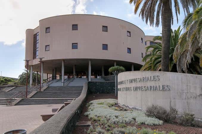 Fachada frontal del edificio con letrero institucional y entorno paisajístico con palmeras