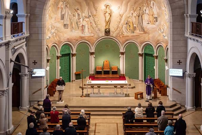 Interior de la capilla del centro con altar, murales religiosos y congregación reunida