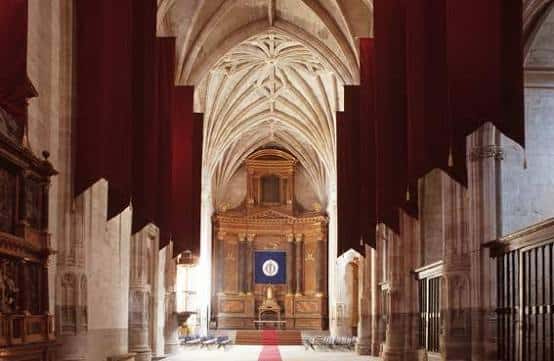 Interior de la iglesia con bóvedas góticas y tapices rojos