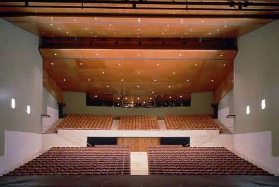 Interior del auditorio con butacas naranjas y techo de madera