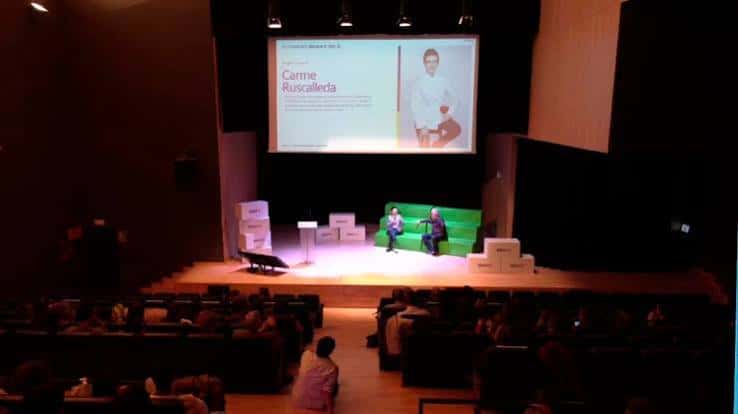 Interior del auditorio en configuración de conferencia con audiencia y panelistas