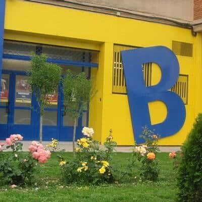 Fachada amarilla de la Biblioteca Pública Municipal con un gran 'B' azul y jardín frontal