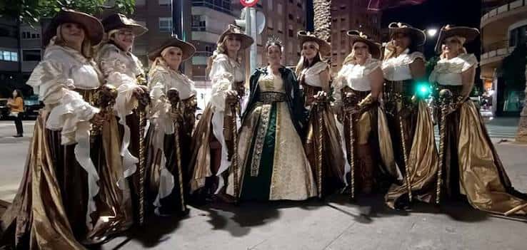 Grupo de mujeres vestidas con trajes tradicionales dorados y blancos durante la celebración nocturna