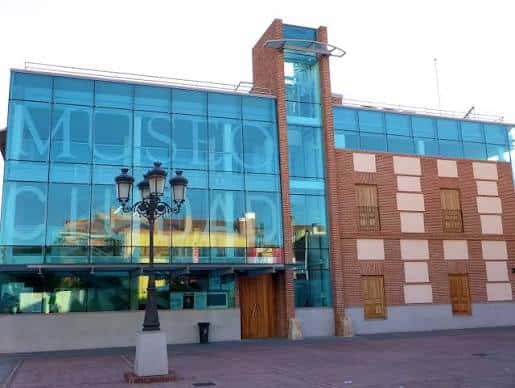 Fachada moderna del Museo de la Ciudad con cristalera azul y torre de ladrillo