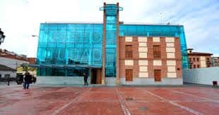 Vista frontal del museo en día soleado, con plaza peatonal y siluetas de visitantes
