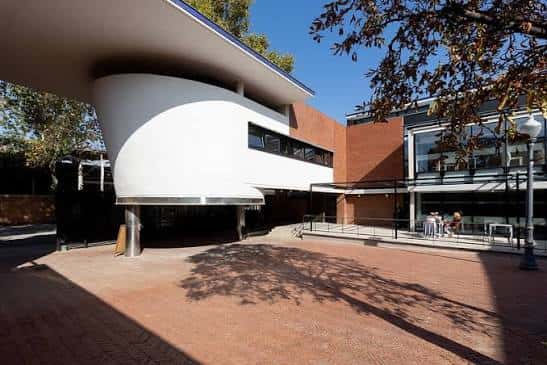 Exterior del centro comunitario en un día soleado, mostrando la plaza de acceso y la arquitectura moderna