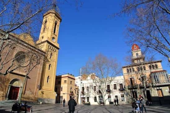 Vista panorámica de la Plaça de la Concòrdia con la Iglesia del Remei y el Centro Cívico Can Deu bajo un cielo azul despejado