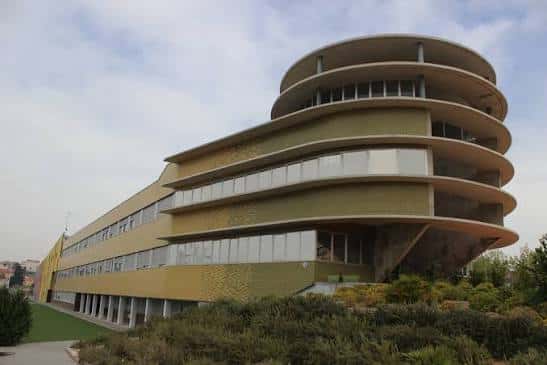 Vista exterior del edificio principal del IES Eduardo Linares Lumeras con su característica arquitectura curva y fachada amarilla