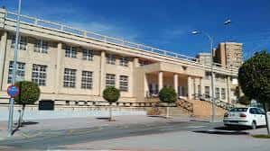 Fachada lateral del edificio deportivo bajo cielo azul, con árboles y aparcamiento frente a él