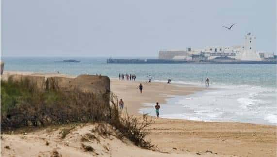 Vista panorámica de la playa con el castillo de San Felipe en el fondo y personas caminando