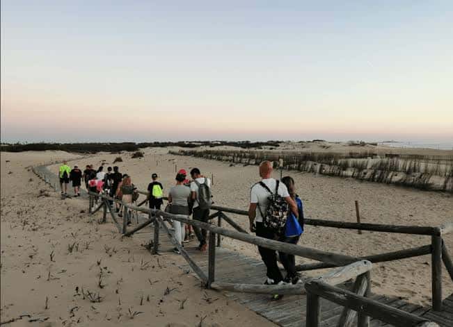 Grupo de excursionistas recorriendo una pasarela de madera al atardecer en la zona dunar