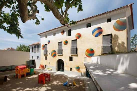 Fachada del Mas Pintat con murales de esferas coloridas y patio infantil