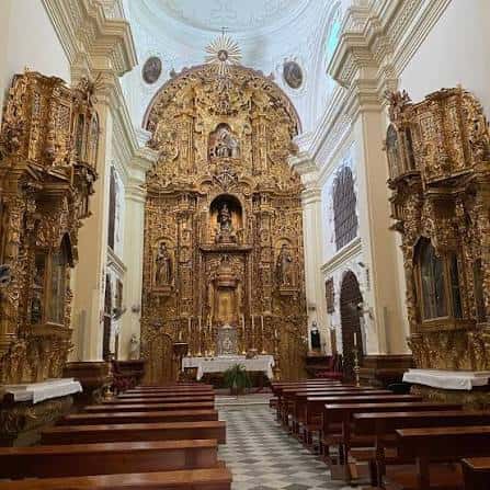 Interior de la capilla con retablo dorado barroco y bancos de madera