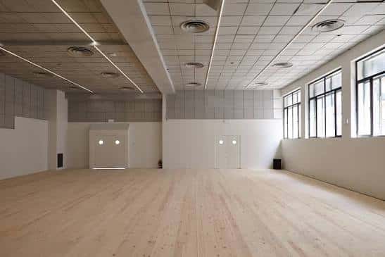 Sala de ensayo vacía con suelo de madera y grandes ventanales