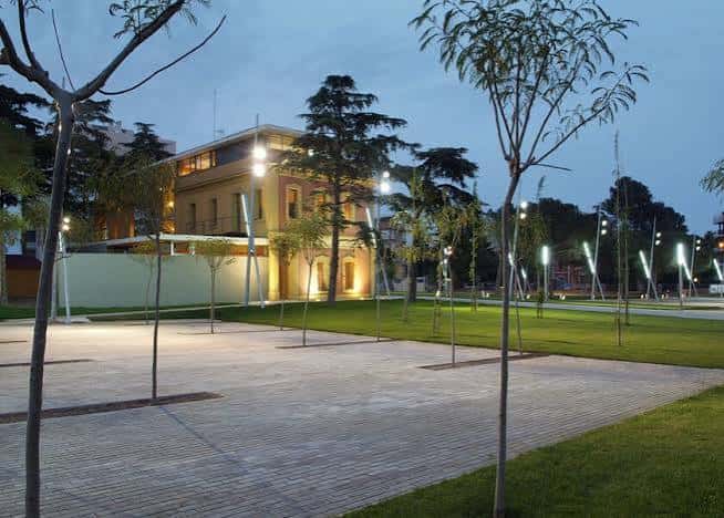Plaza exterior con iluminación moderna y el edificio al fondo en tonos cálidos