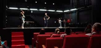 Clase o ensayo en el auditorio con estudiantes actuando frente a público sentado