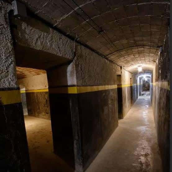 Pasillo subterráneo del refugio con paredes de hormigón y franja amarilla de señalización
