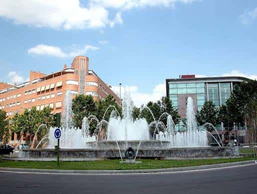 Fuente ornamental en plaza frente a edificios institucionales bajo cielo despejado