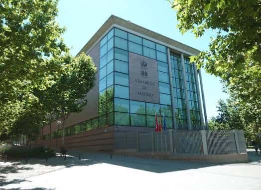 Fachada moderna de la Asamblea de Madrid con cristaleras y escudo institucional