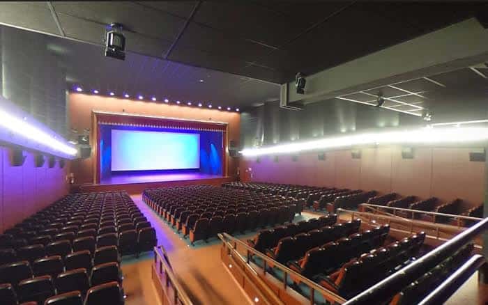 Interior del auditorio configurado para cine con pantalla grande y sistema de iluminación profesional