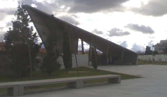 Estructura arquitectónica moderna con techo inclinado y bancos de hormigón en el parque