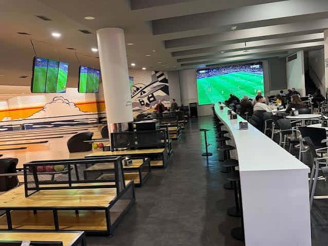 Zona de bar y mesas junto a las pistas de bowling con pantallas deportivas