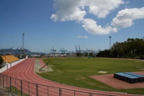 Vista panorámica del estadio con pista de atletismo roja y campo de césped bajo cielo azul