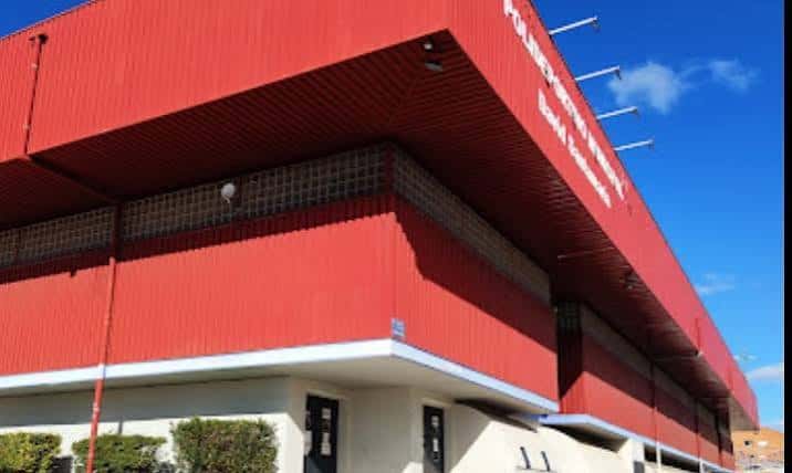 Fachada exterior roja del Polideportivo David Santamaría bajo cielo azul