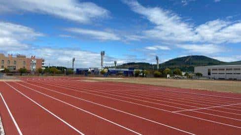 Pista de atletismo desde ángulo cercano mostrando líneas blancas sobre superficie roja bajo cielo azul con nubes dispersas