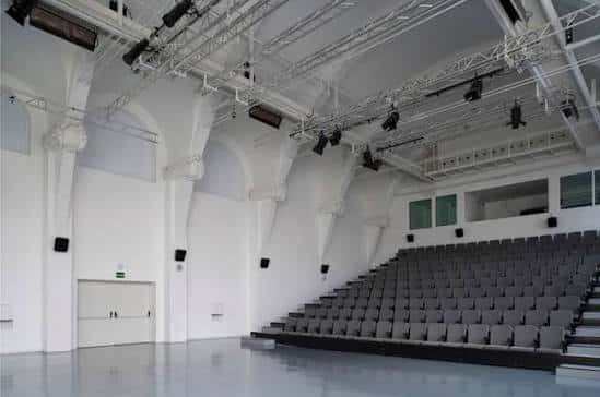 Interior de la sala de espectáculos con gradas blancas y techos altos