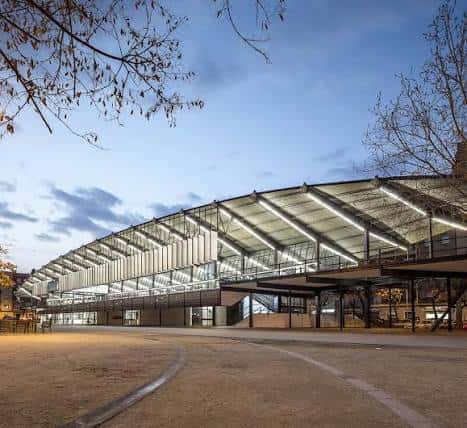 Fachada iluminada del edificio al atardecer, destacando la arquitectura moderna y el espacio público frente a él