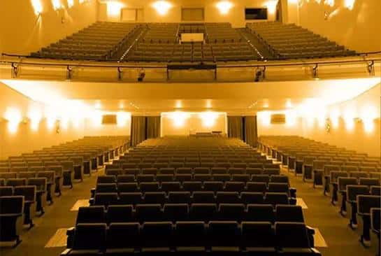 Interior del auditorio con butacas dispuestas en gradas y escenario iluminado